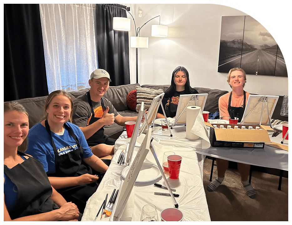 Five people sitting around a table with painting supplies, smiling for the camera.
