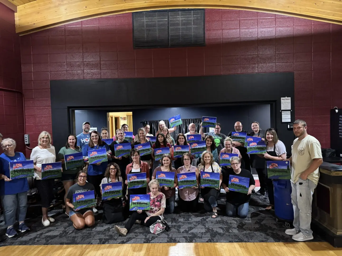 Group holding colorful landscape paintings indoors.